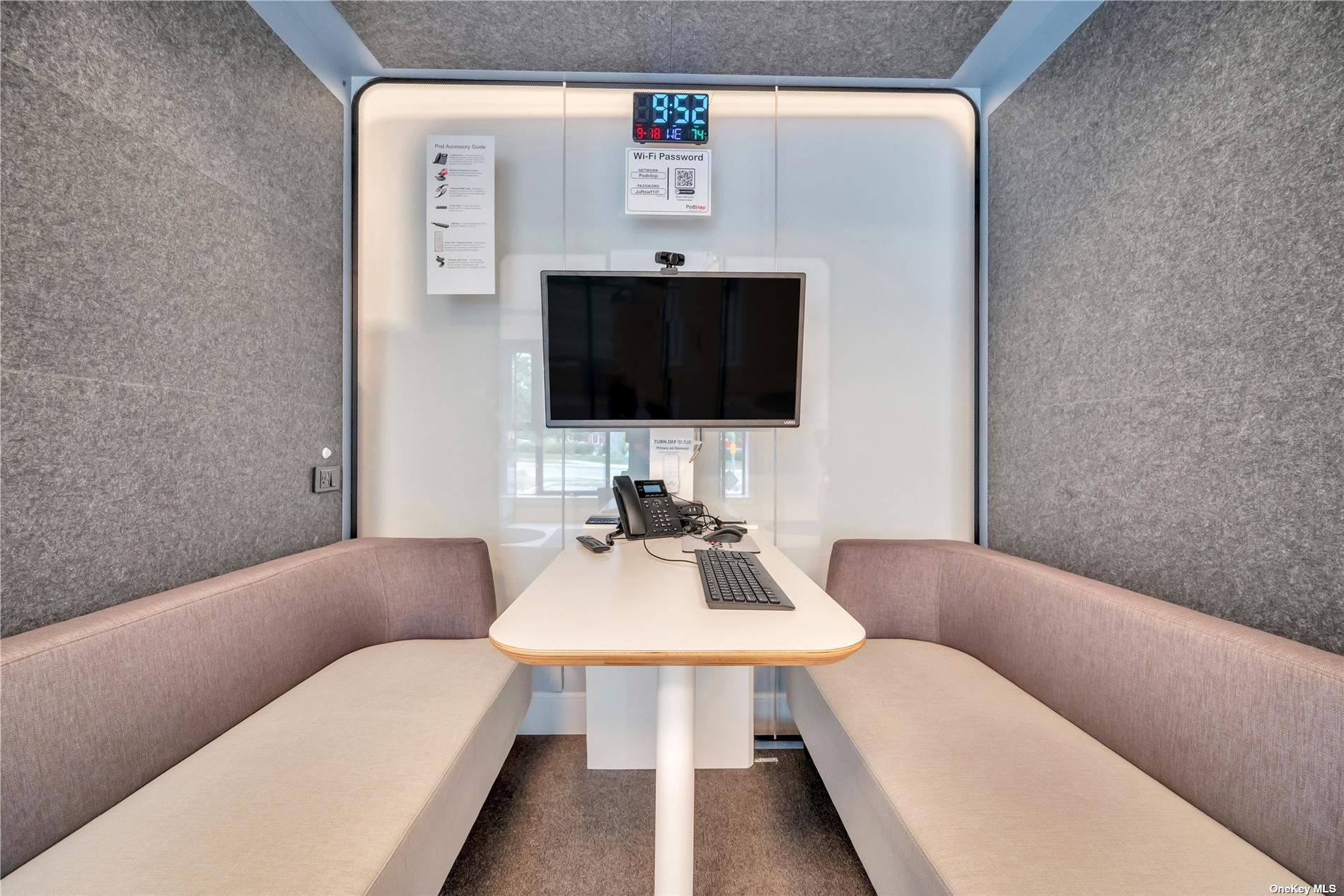 Inside a pod: bench seating, a table, a screen, a webcam, and a phone